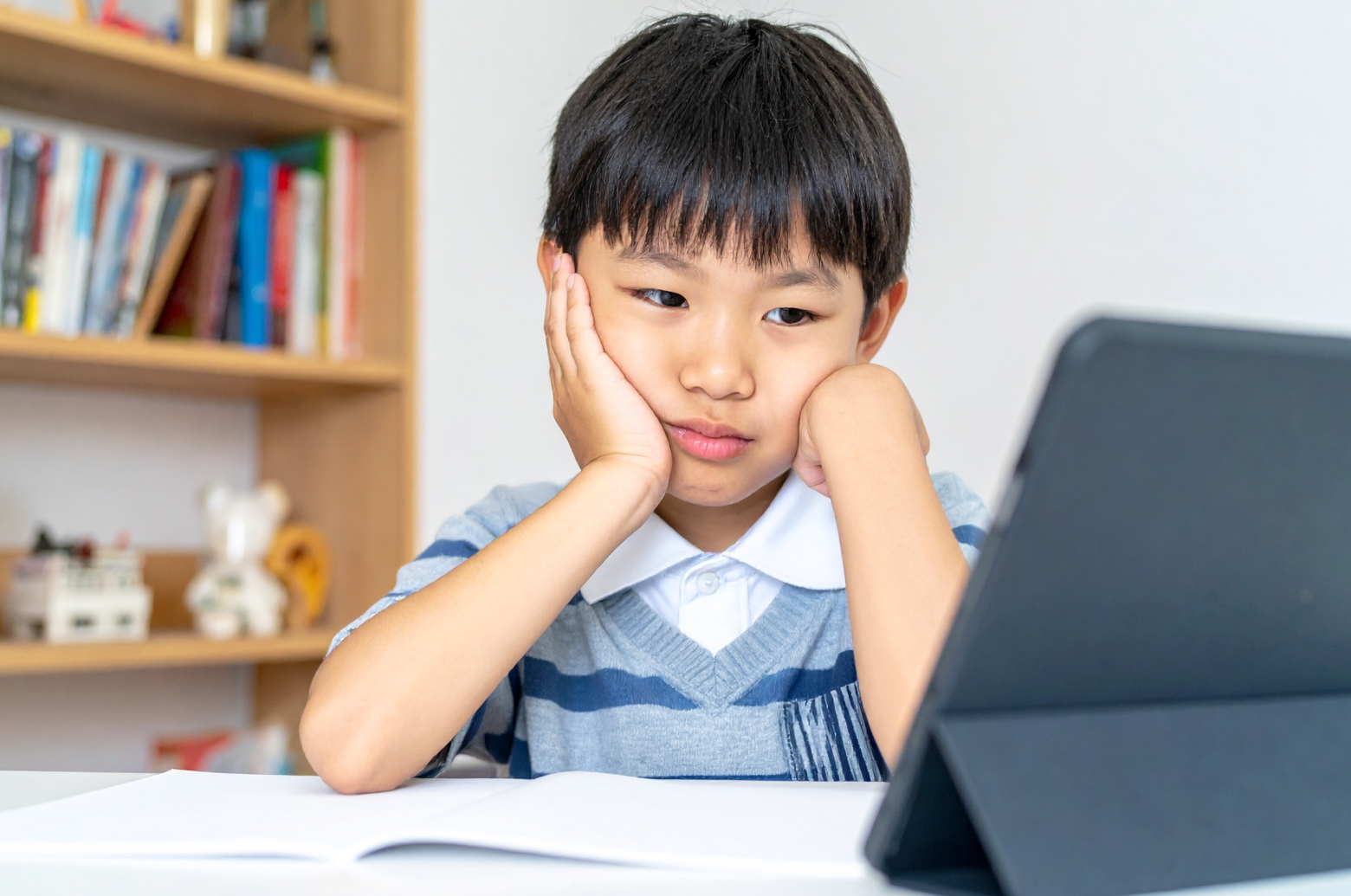 自宅でタブレット教材に取り組んでいるが、明らかにやる気がなさそうな小学生の子ども。片手で頬杖をつき、タブレットをうんざりしたように見ている