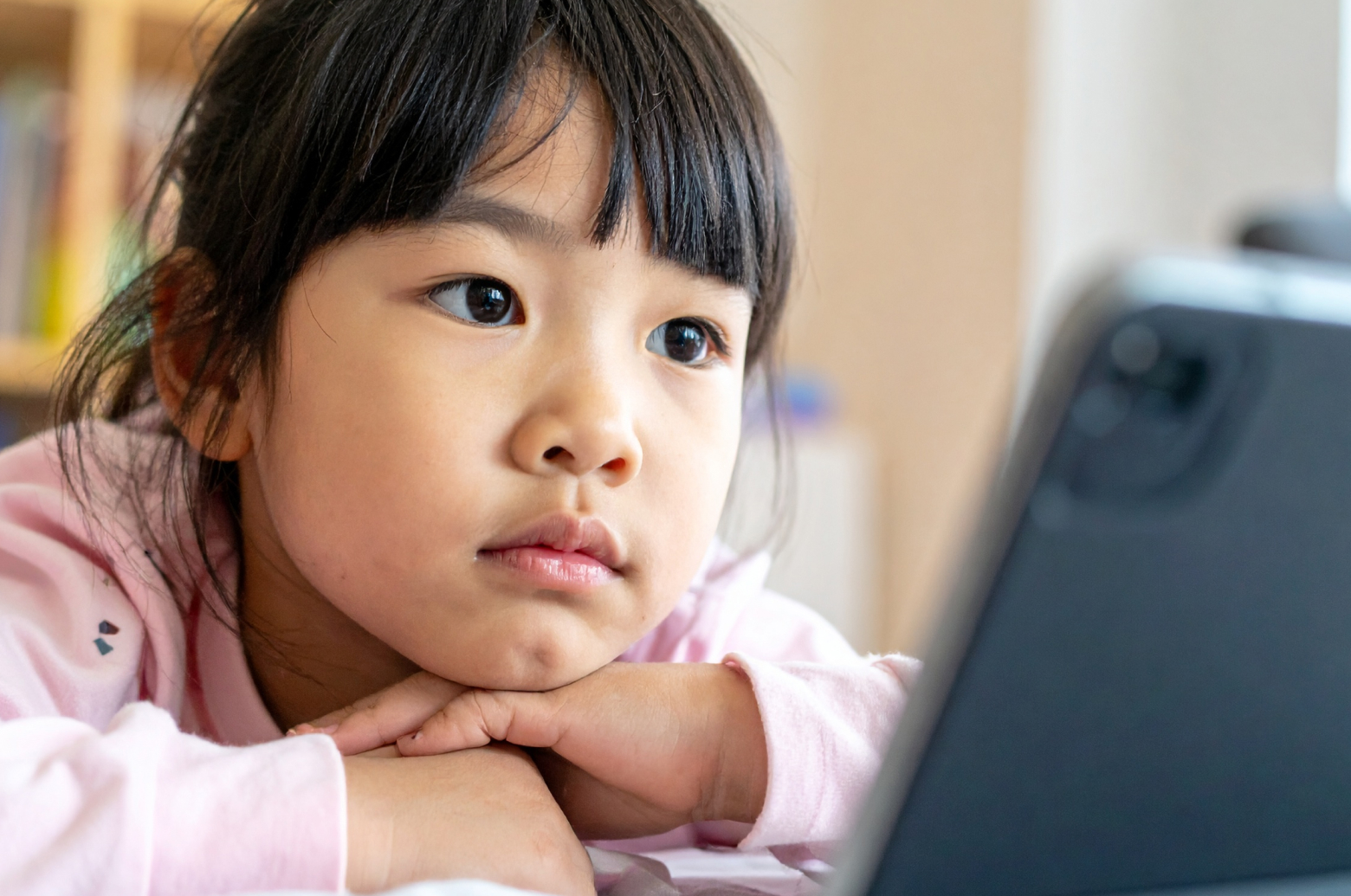 タブレットを使いすぎて、机にうつ伏せになる子ども。目の疲れやストレスが表情や姿勢に出ている
