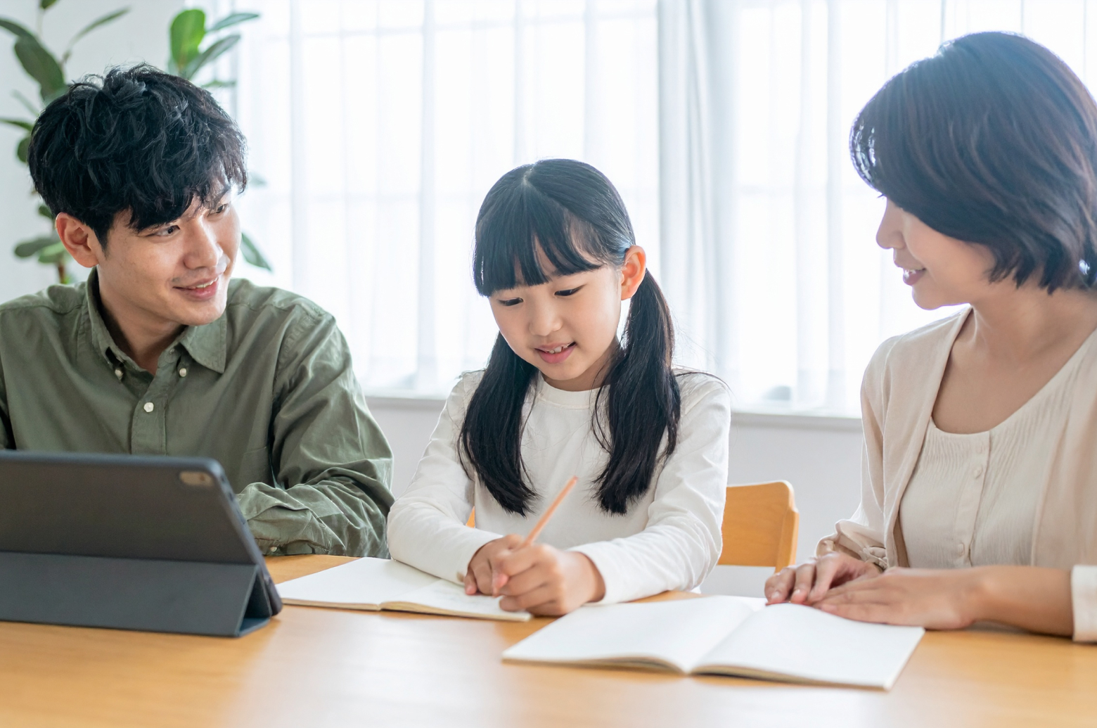 ダイニングテーブルで、親子が一緒にノートやプリントを見ながら、穏やかに話し合っている様子。タブレットは脇に置かれていて、学習方法を見直している雰囲気